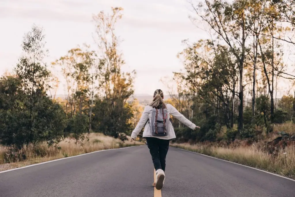 Woman walking down a road alone with a back pack